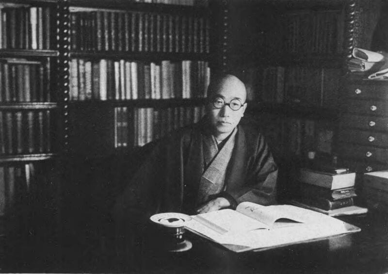 Fotografía de Edogawa Rampo en su estudio, rodeado de libros, con gafas redondas y kimono oscuro, c. 1940-1950